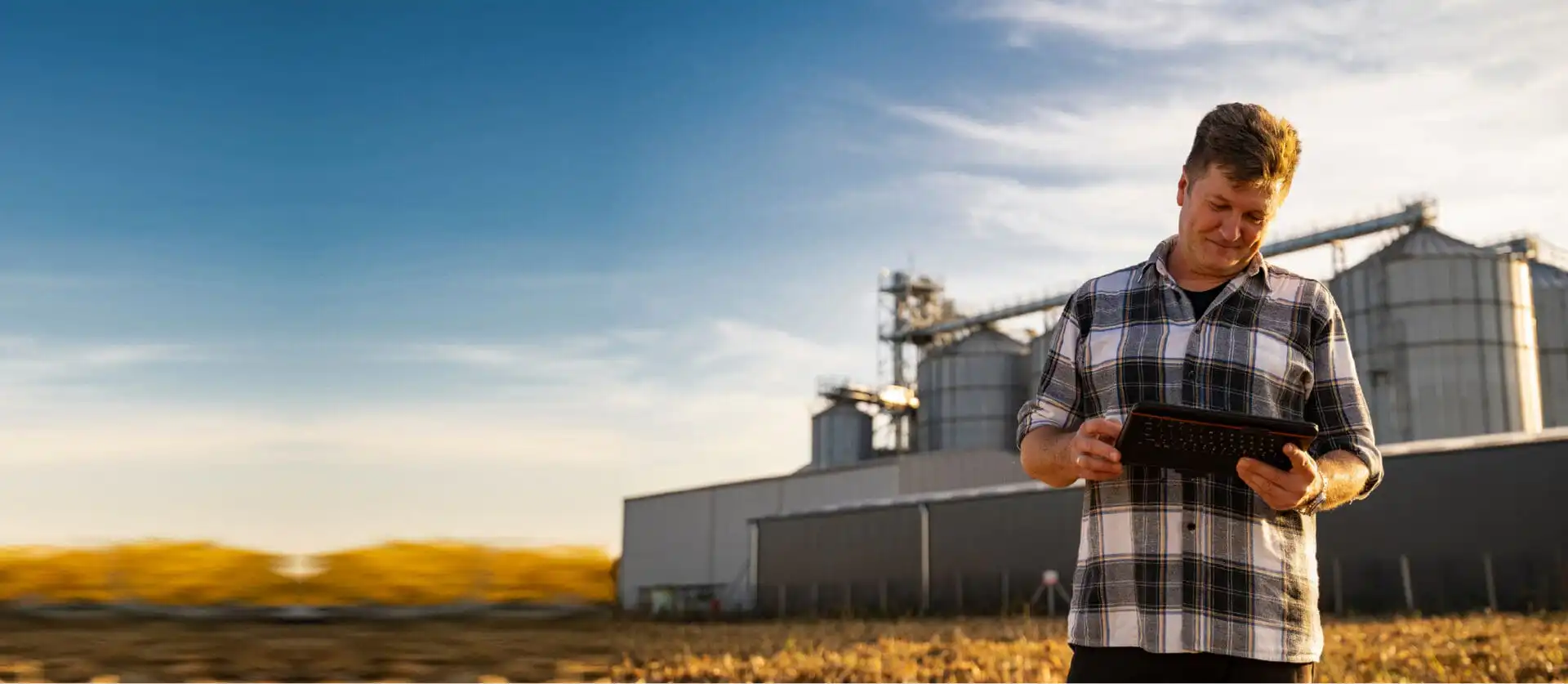 Farmer using tablet near grain silos at sunset