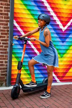 Woman riding electric scooter in front of rainbow mural